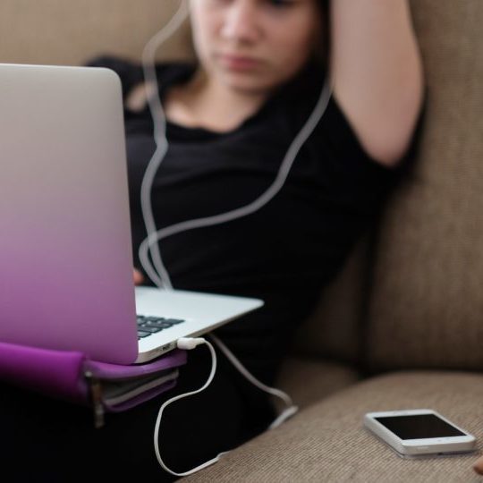 Frau die mit gekrümmten Rücken und Laptop auf dem Sofa liegt.